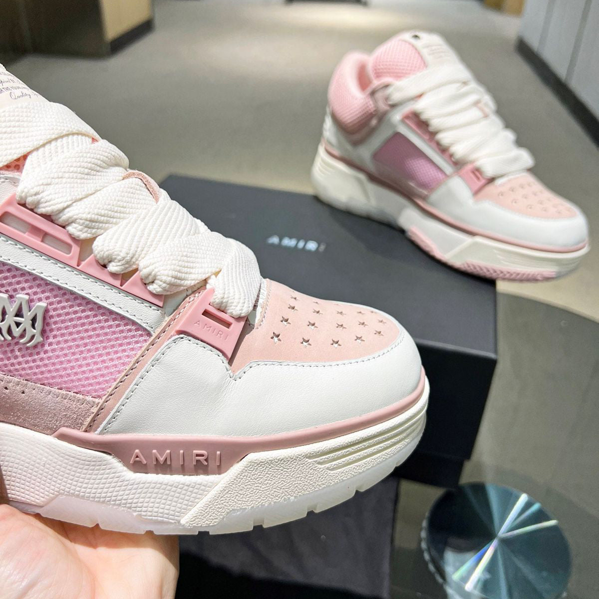 Pink and white sneakers with 'AMIRI' branding on a reflective surface.