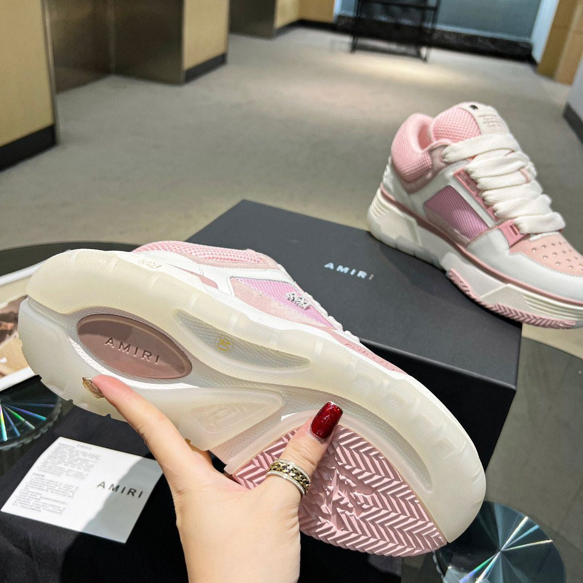 Pink and white sneakers with 'AMIRI' branding on a black surface.
