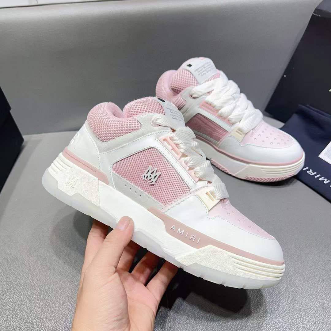 Pink and white sneakers with 'AMIRI' branding held by a hand on a gray surface.